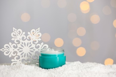 Photo of Jar of hand cream and decorative snowflake on snow against blurred lights, space for text. Winter skin care