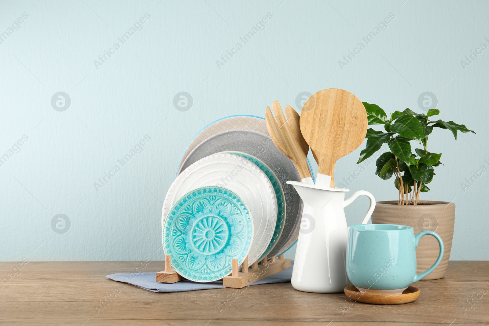 Photo of Potted plant and set of kitchenware on wooden table near light wall, space for text. Modern interior design