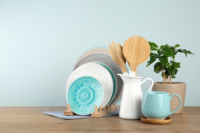 Potted plant and set of kitchenware on wooden table near light wall, space for text. Modern interior design