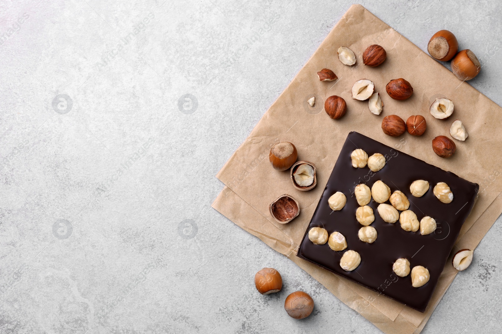 Photo of Delicious chocolate bar and hazelnuts on light grey table, flat lay. Space for text