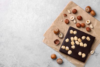 Photo of Delicious chocolate bar and hazelnuts on light grey table, flat lay. Space for text