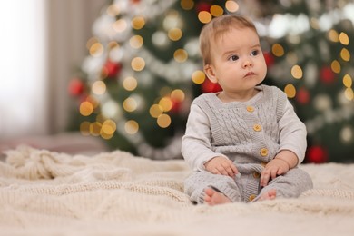 Photo of Cute little baby on knitted blanket against blurred festive lights, space for text. Winter holiday
