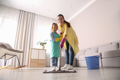 Mother and daughter mopping floor in living room at home