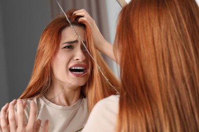 Mental problems. Young woman screaming near broken mirror indoors