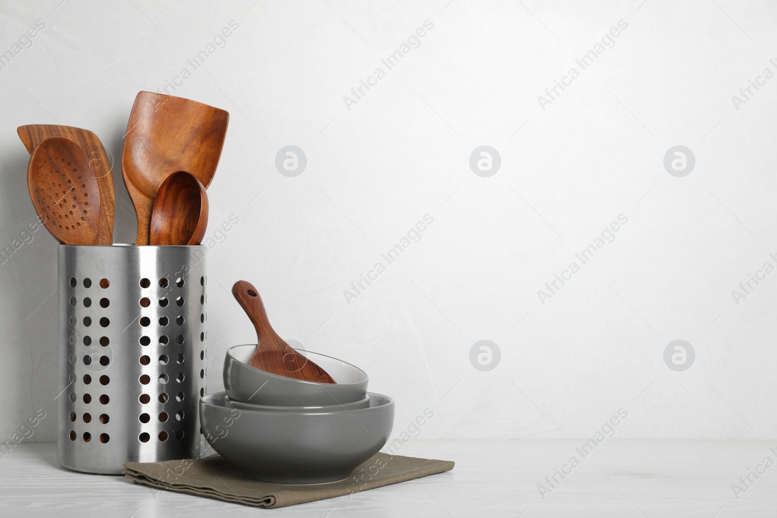 Photo of Set of wooden kitchen utensils and bowls on white table. Space for text