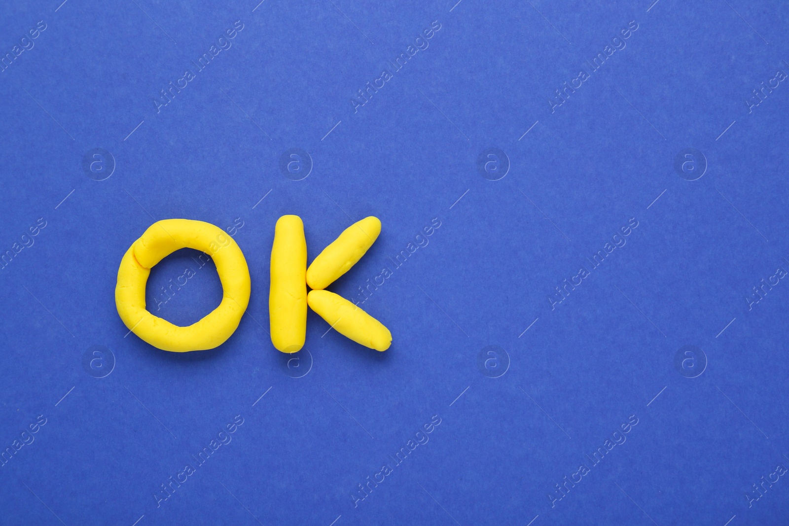 Photo of Word Ok made of yellow plasticine on blue background, top view. Space for text