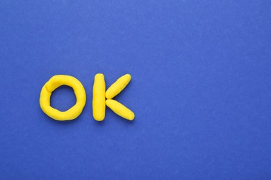 Photo of Word Ok made of yellow plasticine on blue background, top view. Space for text