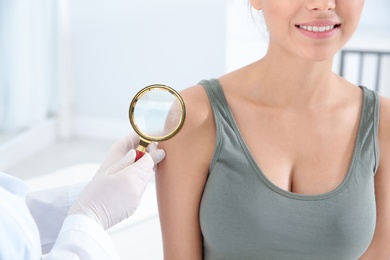 Dermatologist examining patient's birthmark with magnifying glass in clinic, closeup