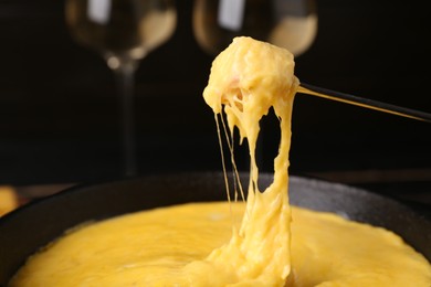 Dipping piece of ham into fondue pot with melted cheese on table, closeup