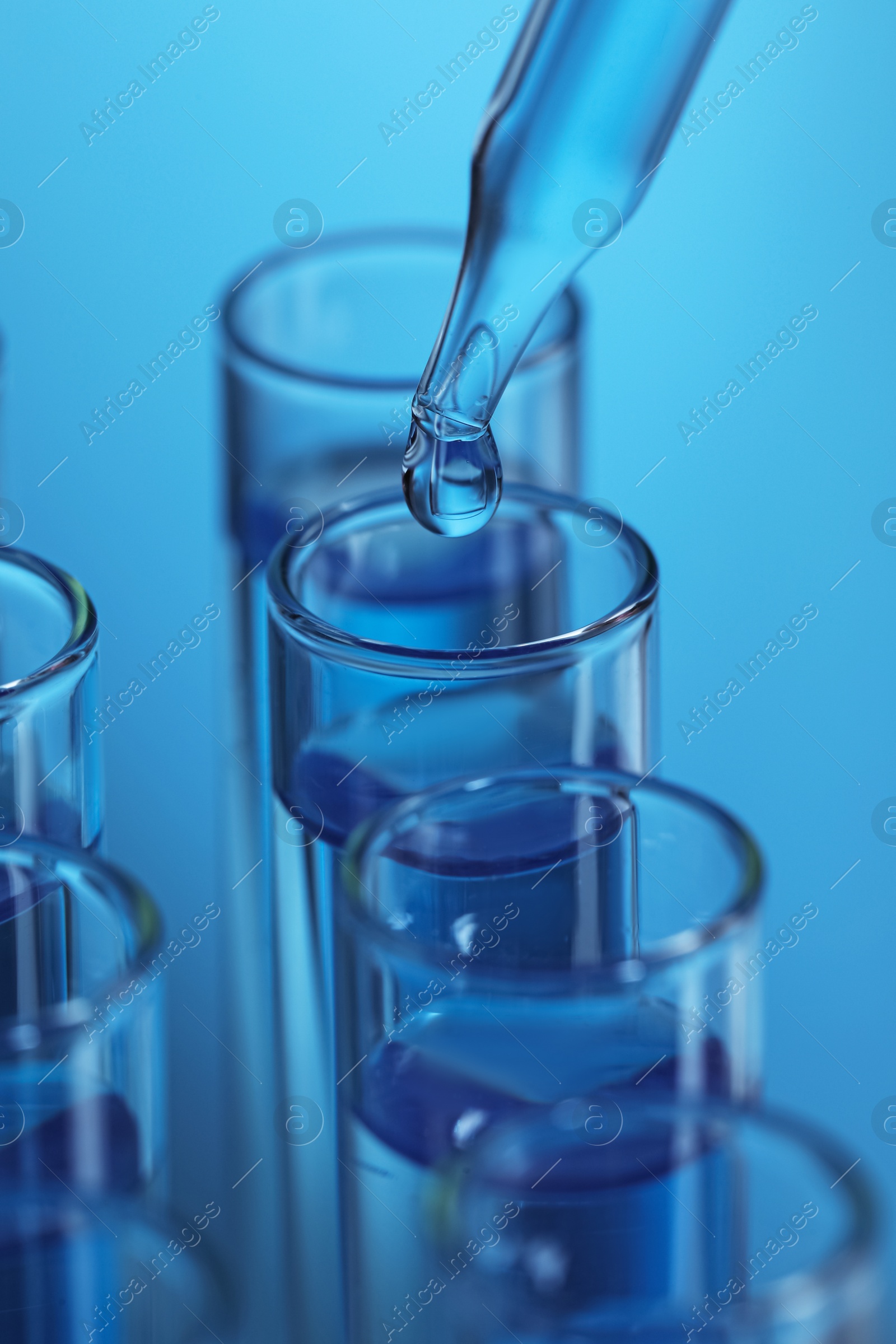 Photo of Dripping reagent into test tube on light blue background, closeup. Laboratory analysis