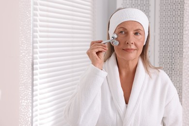 Photo of Woman massaging her face with metal roller near mirror in bathroom. Space for text