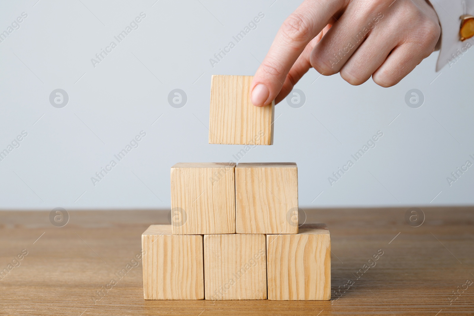 Photo of Woman building pyramid of cubes on wooden table against light background, closeup. Space for text