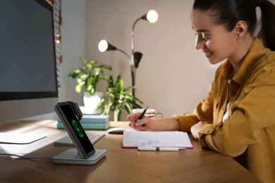 Woman at desk, smartphone and watch on wireless charger. Modern workplace