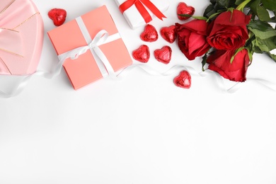 Photo of Heart shaped chocolate candies, roses and gift boxes on white background, top view. Valentine's day celebration