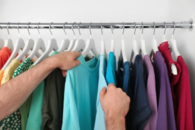 Photo of Man choosing clothes from rack in wardrobe, closeup