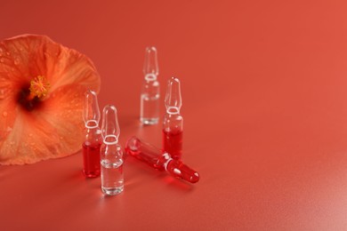Photo of Skincare ampoules and hibiscus flower on coral background. Space for text