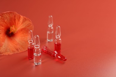 Skincare ampoules and hibiscus flower on coral background. Space for text