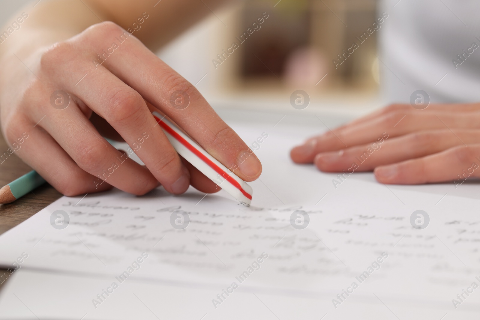 Photo of Girl erasing mistake in her notebook at wooden desk, closeup