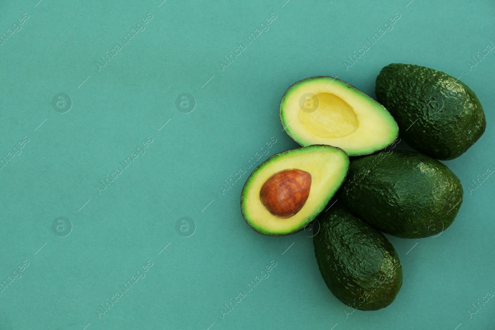 Photo of Tasty whole and cut avocados on turquoise background, top view. Space for text