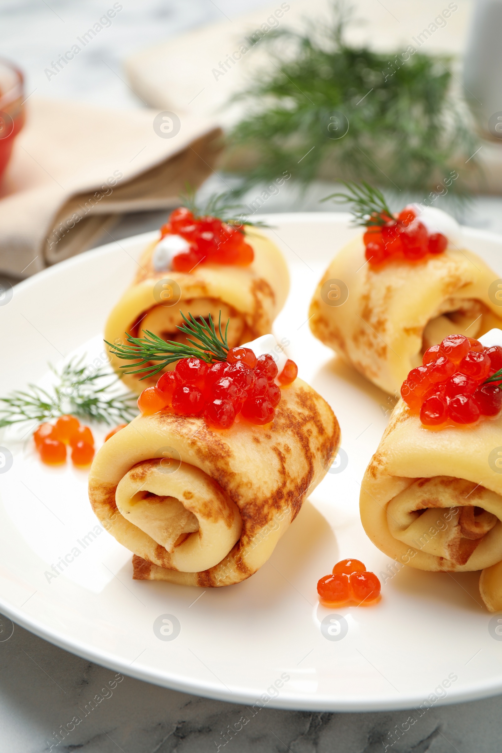 Photo of Delicious thin pancakes with red caviar on white marble table, closeup