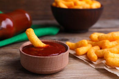 Tasty cheesy corn stick in bowl with red sauce on wooden table, closeup