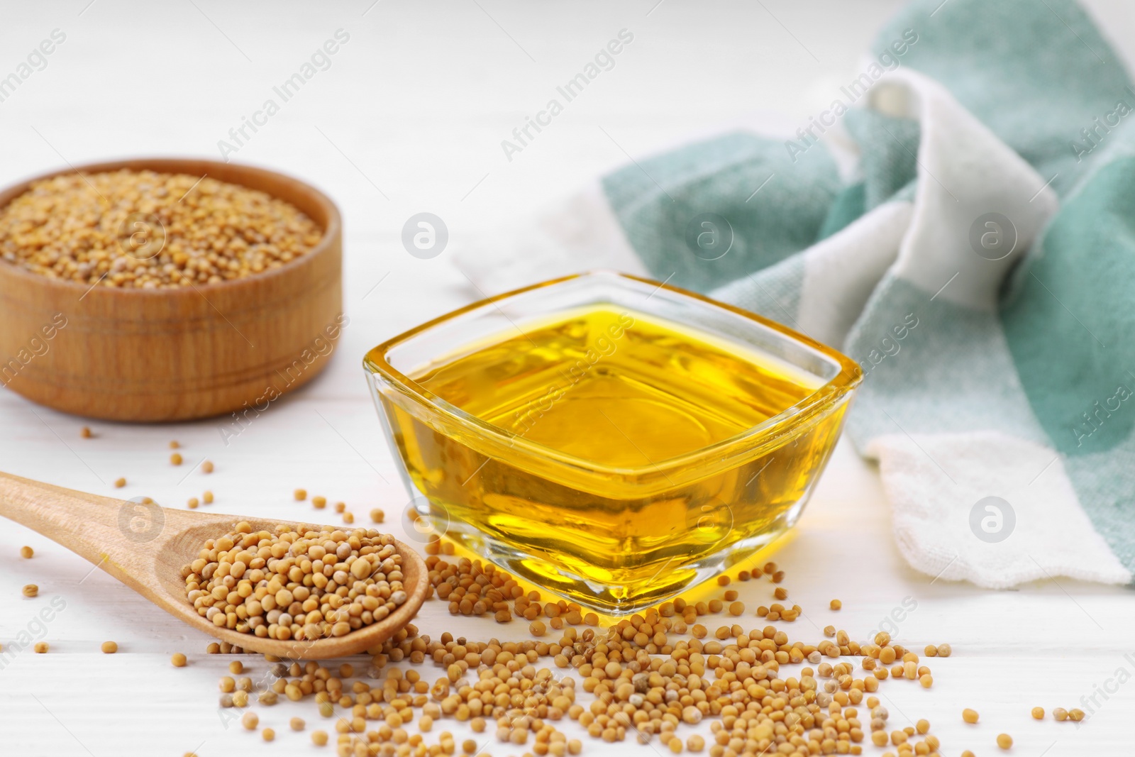 Bowl of natural oil and mustard seeds on white wooden table Photo of Bowl of natural oil and mustard seeds on white wooden table
