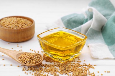 Photo of Bowl of natural oil and mustard seeds on white wooden table