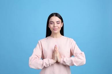 Young woman meditating on light blue background. Stress relief exercise