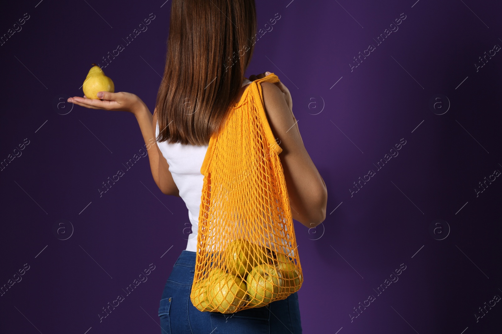 Photo of Woman holding net bag with fresh ripe pears on purple background, closeup