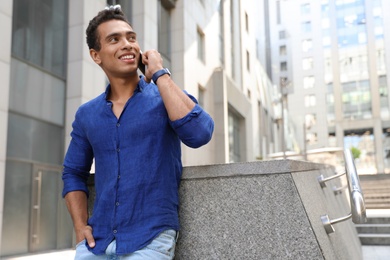Handsome young African-American man talking on mobile phone outdoors. Space for text