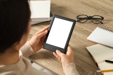 Photo of Young woman using e-book reader at wooden table, closeup