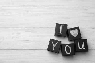 Photo of Black cubes with chalk written words I LOVE YOU on white wooden table, flat lay. Space for text