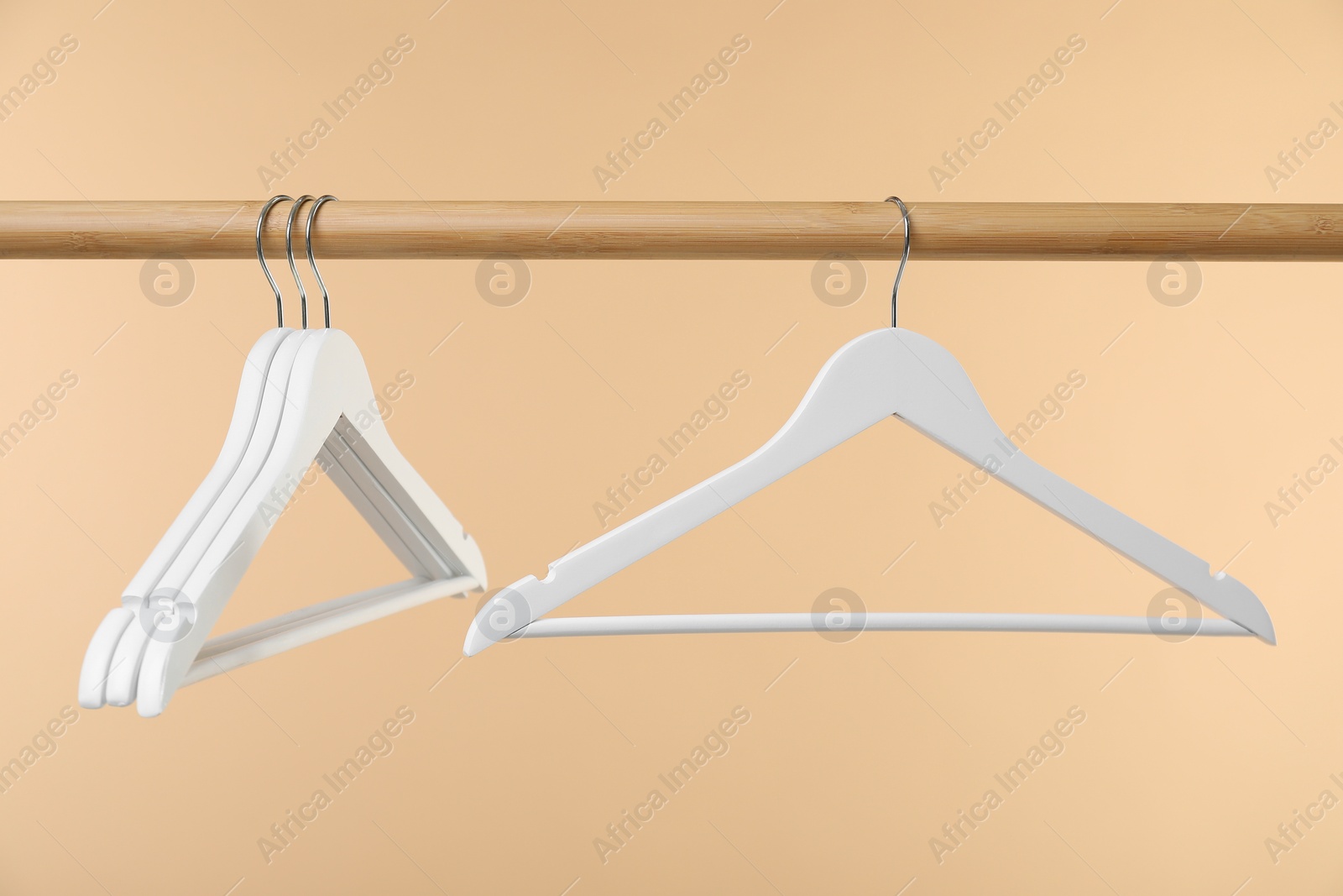 Photo of Empty clothes hangers on wooden rack against beige background