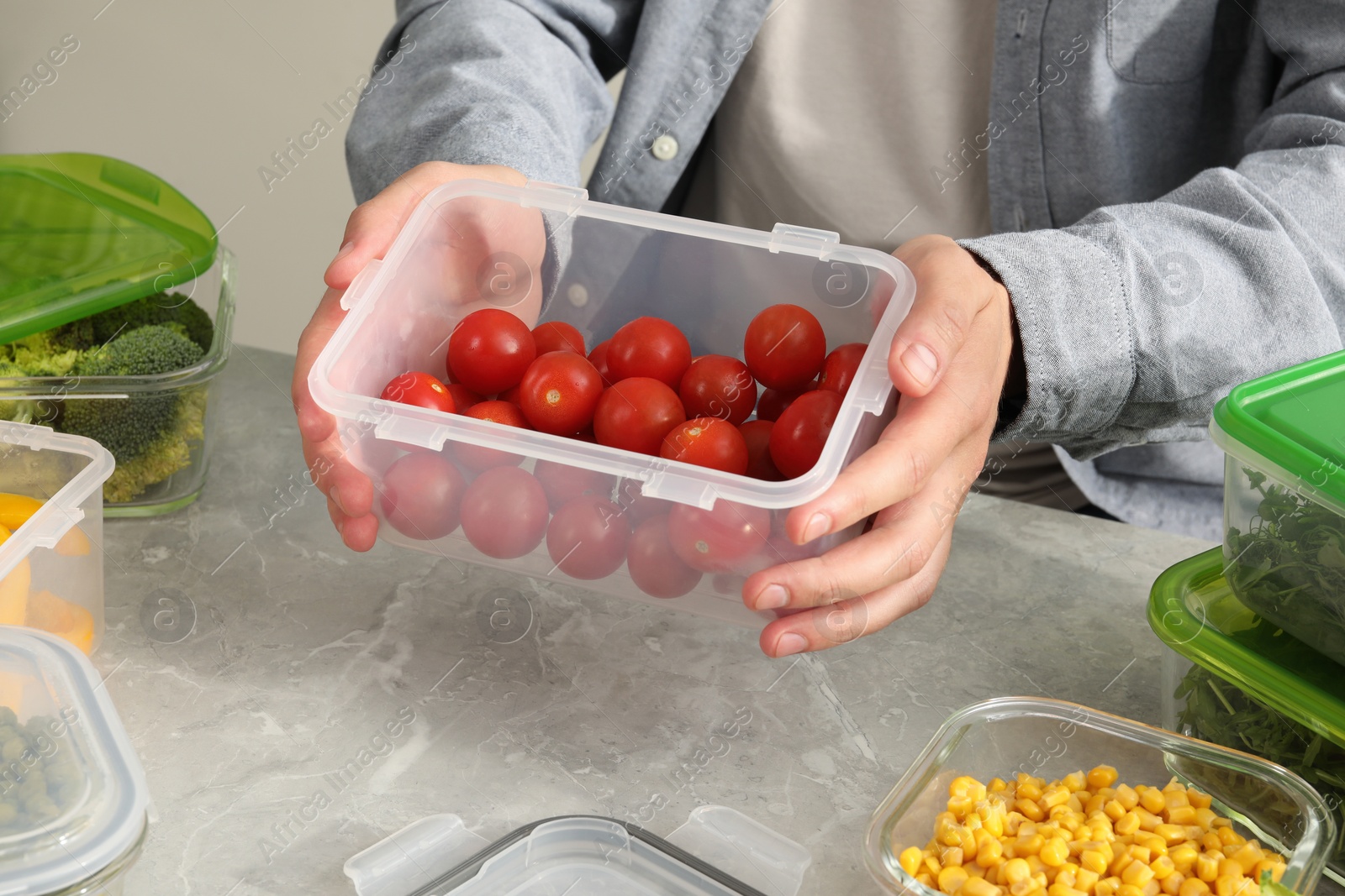 Photo of Man holding plastic container with fresh cherry tomatoes at light grey table in kitchen, closeup. Food storage