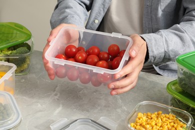 Photo of Man holding plastic container with fresh cherry tomatoes at light grey table in kitchen, closeup. Food storage