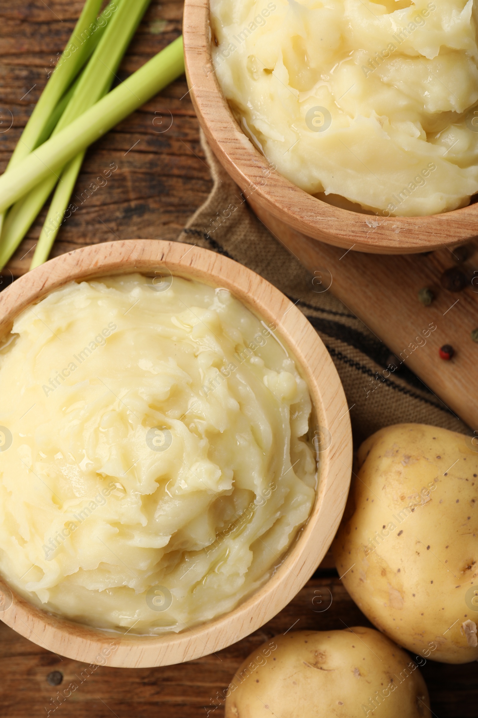 Photo of Bowls of tasty mashed potato, pepper and leeks on wooden table, flat lay