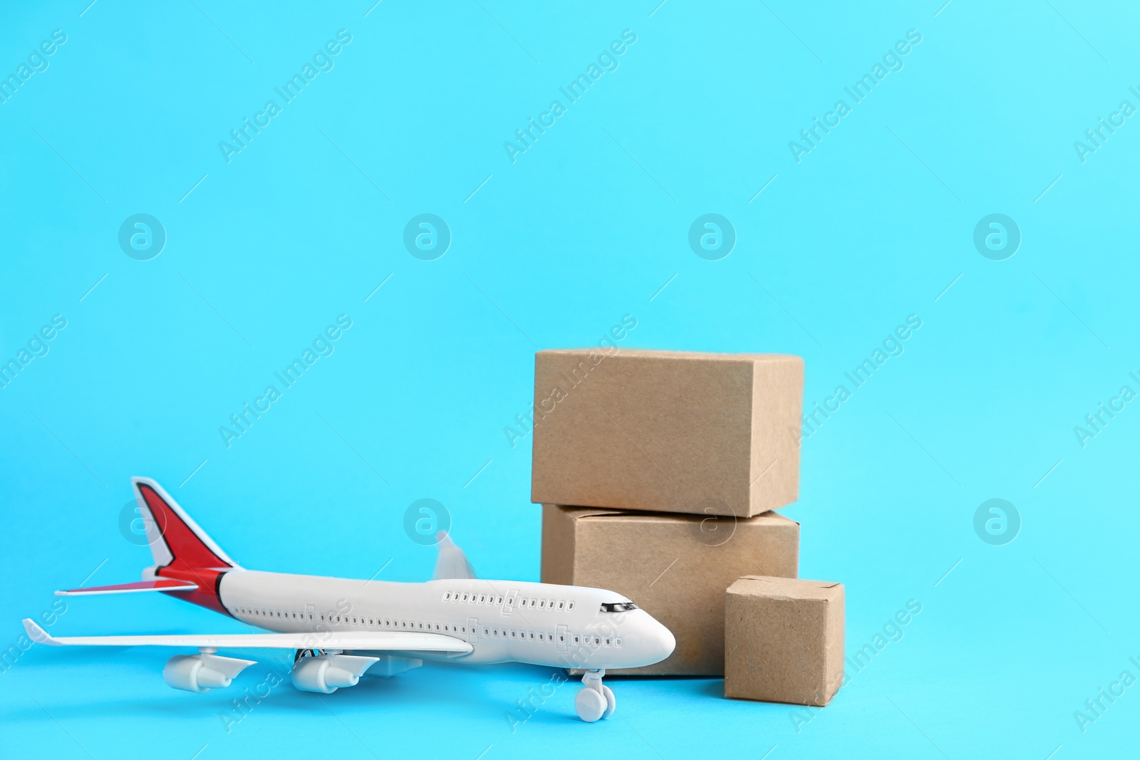 Photo of Airplane model and carton boxes on light blue background. Courier service