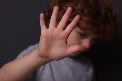 Photo of Child abuse. Boy making stop gesture near grey wall, selective focus
