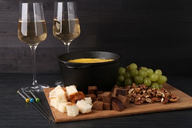 Photo of Fondue pot with melted cheese, glasses of wine and different products on black wooden table