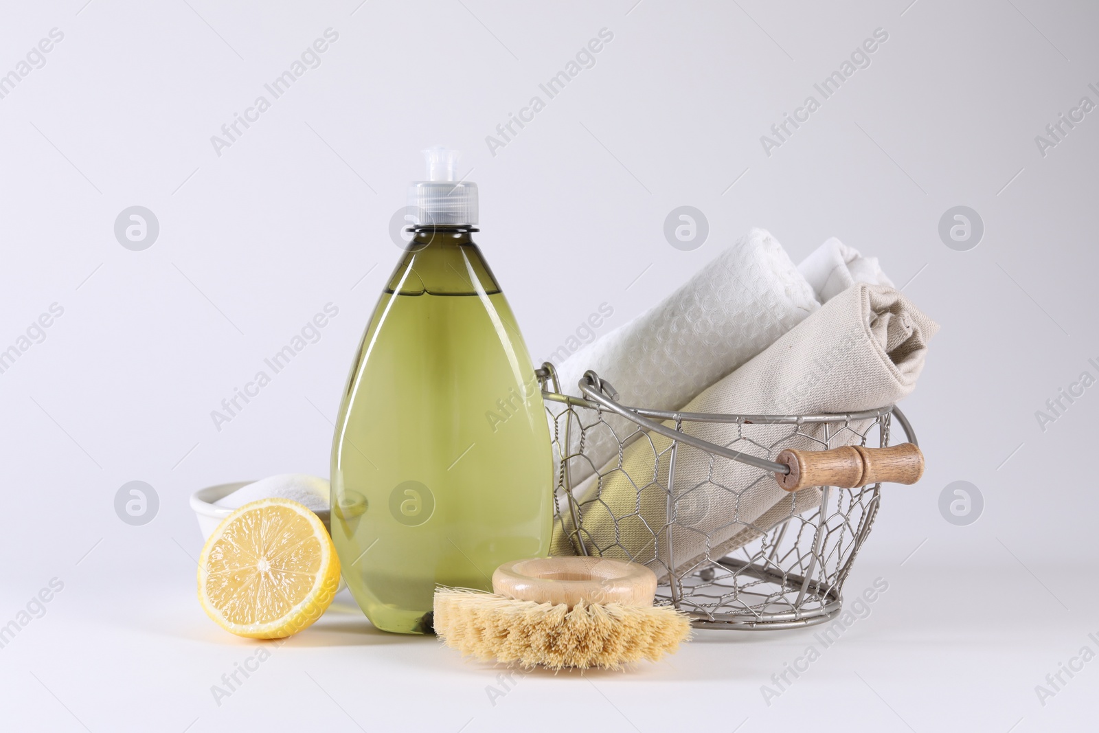 Photo of Bottle of cleaning product, brush, rags and lemon on light background