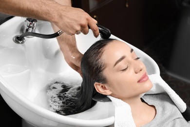 Stylist washing client's hair at sink in beauty salon