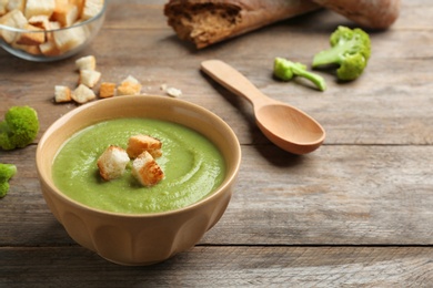 Bowl of broccoli cream soup with croutons served on wooden table, space for text