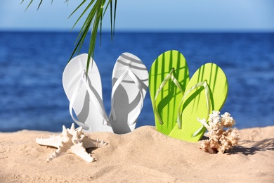 Composition with bright flip flops on sand near sea in summer. Beach accessories