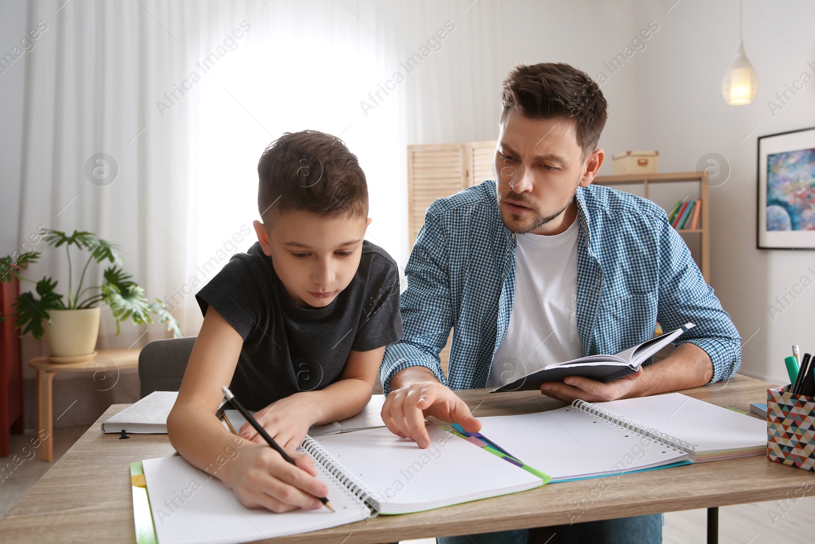 Photo of Dad helping his son with homework in room