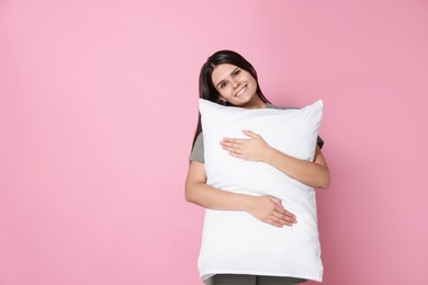 Photo of Happy young woman hugging soft pillow on pink background, space for text