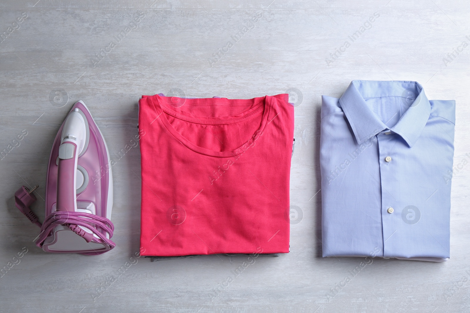 Photo of Flat lay composition with folded clothes and modern iron on light table