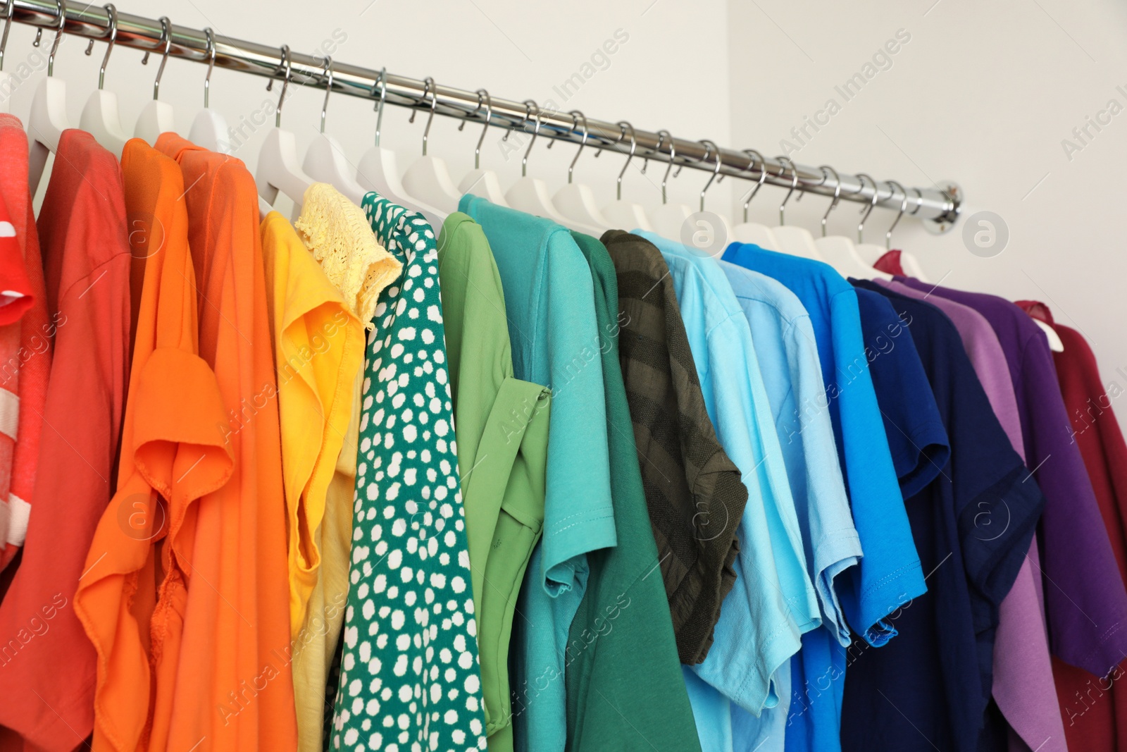 Photo of Hangers with different colorful clothes on rack in wardrobe