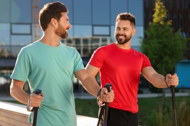 Happy men practicing Nordic walking with poles outdoors on sunny day