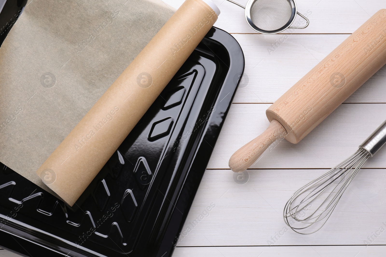 Photo of Baking pan with parchment paper and kitchen utensils on white wooden table, flat lay