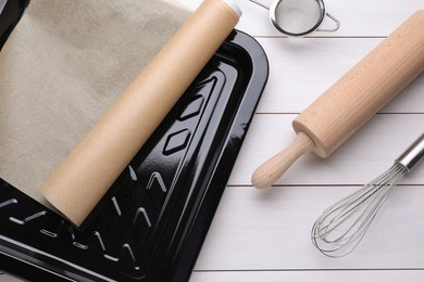 Baking pan with parchment paper and kitchen utensils on white wooden table, flat lay